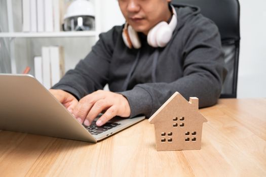 Selective focus of wooden house, Smiling businessman typing on the computer for send email. Concept of working from home until Coronavirus (COVID-19) quarantine, happily freelance working lifestyle