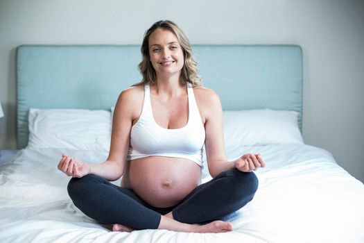 Pregnant woman doing yoga on her bed