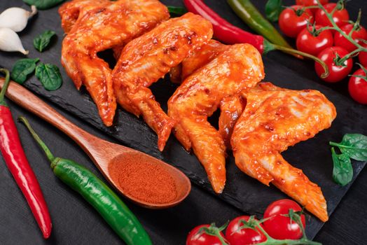 Raw chicken wings in a marinade with spices on a black plate. Top view. Chicken meat close-up.