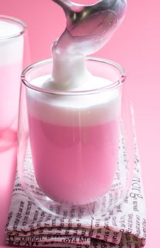 Summer drink concept. Pour froth milk on strawberry pink milk in clear glass on pink background. 