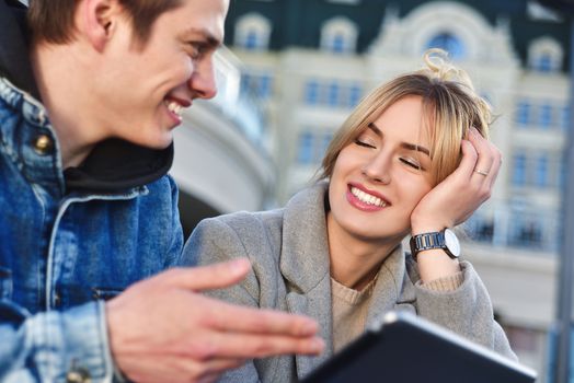 Attractive young couple sitting on floor in urban street reading information on a tablet with a smile