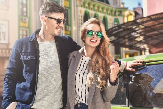 Couple enjoy the sunny mood standing near the car