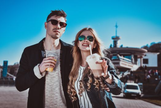 Smiling couple walk at the street in weekend and drink some cocktails.