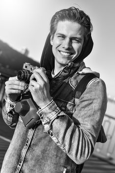 Stylish man photographing on retro camera. Tourist stay on the bridge and make a photo.