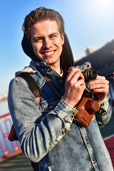 Stylish man photographing on retro camera. Tourist stay on the bridge and make a photo.