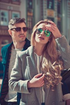 Fashionable couple in sunglasses stand at street near the car