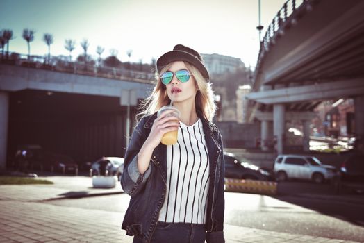 Beautiful girl with juice in sunglass walking at the street on urban style
