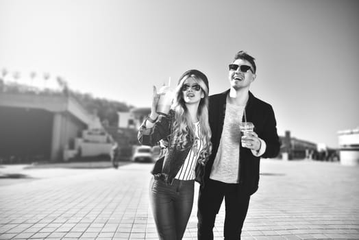 Smiling couple walk at the street in weekend and drink some cocktails.