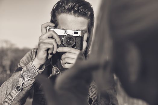 Stylish man photographing a woman on retro camera in the street