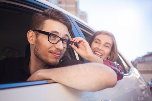 Enjoying travel. Beautiful young couple sitting on the front passenger seats and smiling while handsome man driving a car.