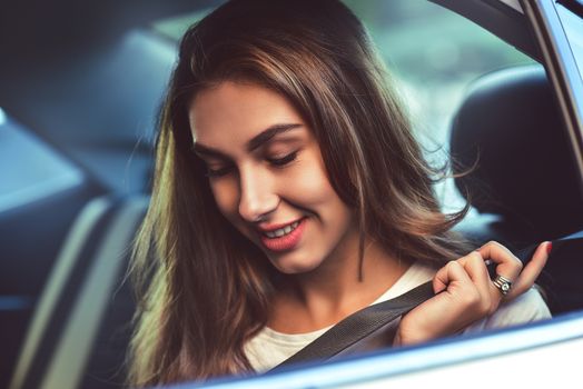 Beautiful woman with phone smiling while sitting on the back seat in the car.