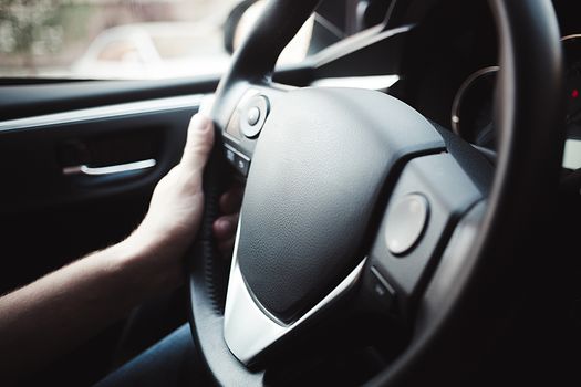 Male arms holding leathern rudder of car