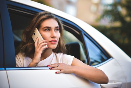 Beautiful woman with phone smiling while sitting on the back seat in the car.