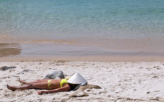woman sexy in bikini and chinese conical straw hat relaxing at white sand beach at the clear blue waters