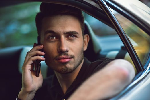 Handsome man sit in the back seat of the car and use a phone.