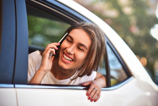 Beautiful woman with phone smiling while sitting on the back seat in the car.