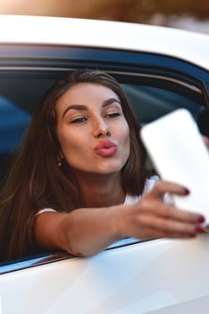 Young woman in the car going on holiday as a passenger makes selfie.