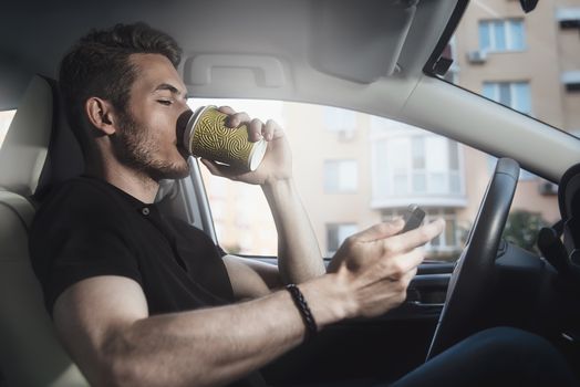 Man arms hold a coffee and phone in automobile