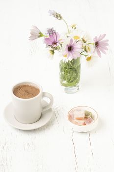 Cup of coffee and Turkish delights on a wooden table with colorful spring flowers on