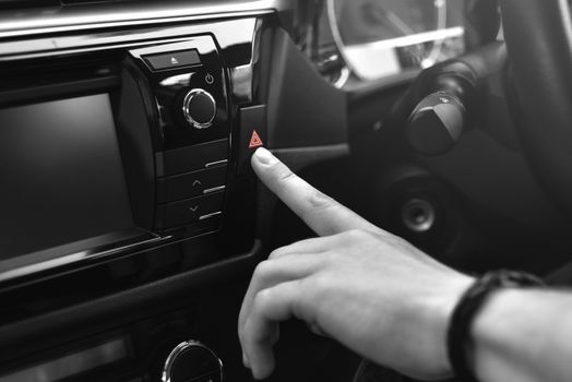 man sits in car and push on red emergency button, black and white