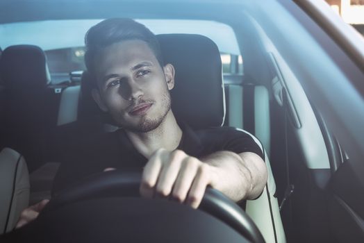 Handsome man sitting in a car and holding steering wheel.