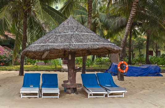 Blue sunbeds Deckchairs, umbrella, parasol and Life buoy on the tropical sand beach. Palm trees at tropical coast.