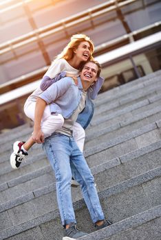 Man giving his pretty girlfriend a piggy back at street smiling at each other on a sunny day.