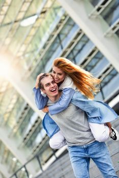 Man giving his pretty girlfriend a piggy back at street smiling at each other on a sunny day.