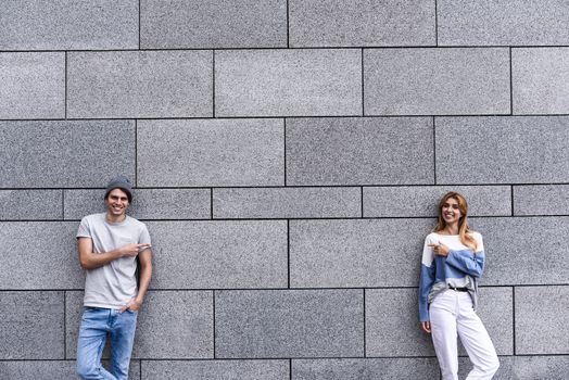 Cheerful couple at the street, show a big sale, or nice offer. Advertise concept. People, travel and tourism - on city street and couple show with their fingers something over gray wall background.