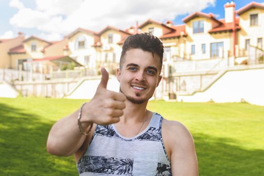 Attractive resting man with thumb up. beautiful cottages in the background
