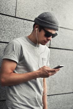 People, technology, travel and tourism - man with earphones, smartphone on city street and listening to music over gray wall background