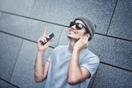 People, technology, travel and tourism - man with earphones, smartphone on city street and listening to music over gray wall background