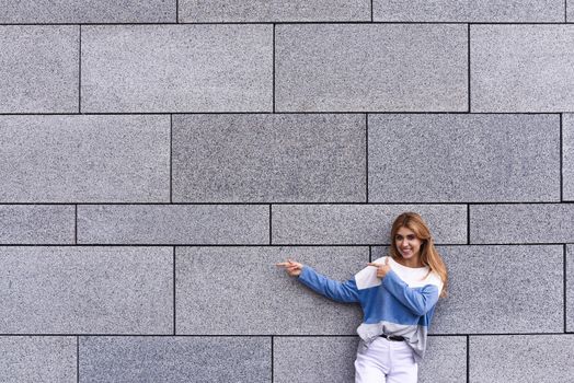 Cheerful girl at the street, show a big sale, or nice offer. Advertise concept. People, travel and tourism - woman on city street and girl show with her finger something over gray wall background