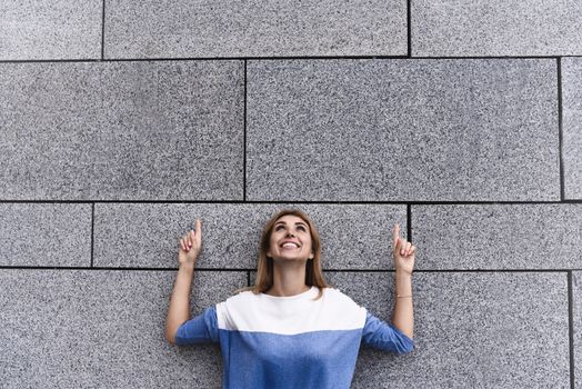 Cheerful girl at the street, show a big sale, or nice offer. Advertise concept. People, travel and tourism - woman on city street and girl show with her fingers something over gray wall background