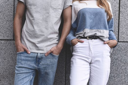 Two friends leaning to a wall and ignoring each other. , guy and a woman in gray wall background.