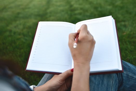 close up young women writing on notebook in park. education and knowledge concept