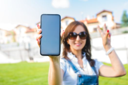 Portrait of a happy excited casual woman pointing with her finger at blank screen mobile phone isolated over gray background. Copy space.