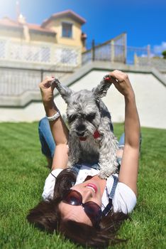 Pretty adult caucasian happy woman resting in the park on a sunny day with her beloved dog. Female lay on the grass smiling and looking at the camera