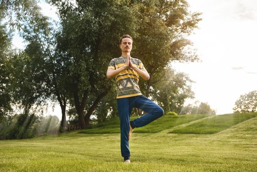 Fitness man doing exercise on one leg isolated in the park. enjoying nature, yoga and meditation concept. spiritual practices.