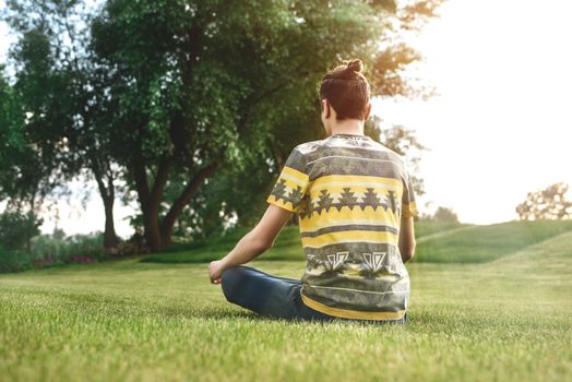 Young man meditating outdoors in the park, sitting with eyes closed and his hands together