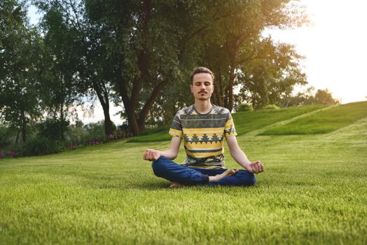 Young man meditating outdoors in the park, sitting with eyes closed and his hands together