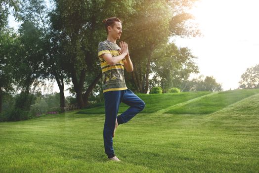 Fitness man doing exercise on one leg isolated in the park. enjoying nature, yoga and meditation concept. spiritual practices.