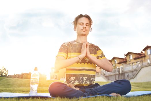 Young man meditating outdoors in the park, sitting with eyes closed and his hands together