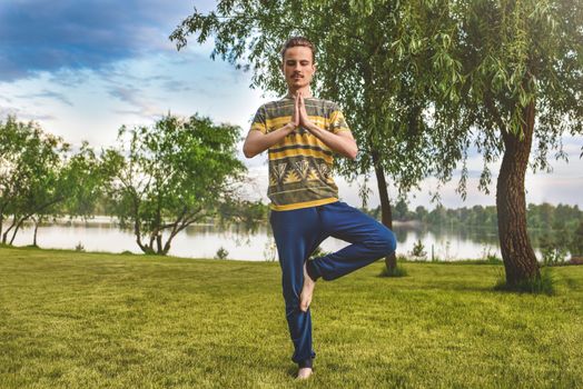 Fitness man doing exercise on one leg isolated in the park. enjoying nature, yoga and meditation concept. spiritual practices.