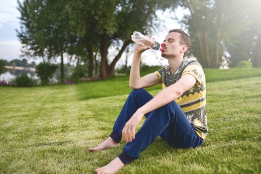 Young man sitting on the garden and drinking water after running