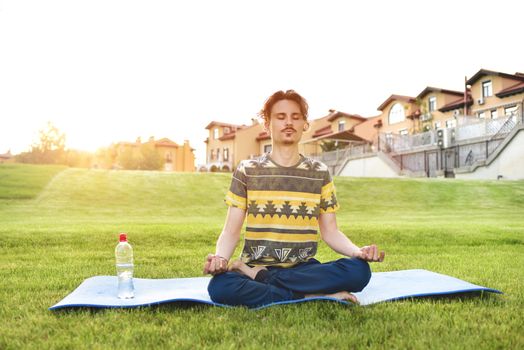 Young man meditating outdoors in the park, sitting with eyes closed and his hands together