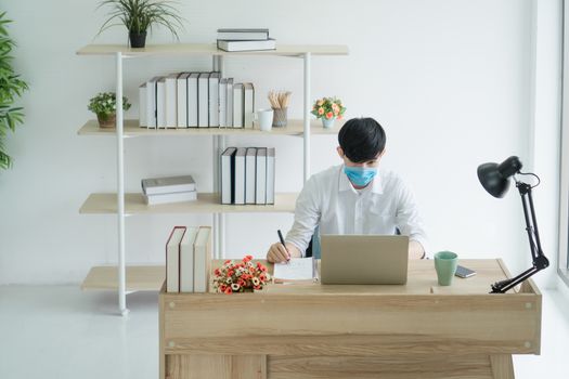 A young Asian man wears a medical mask to work from home. Is a distance from society To prevent the spread of Corona virus