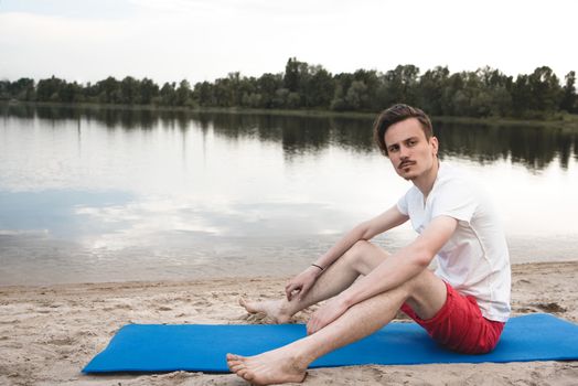 Young man relax siting on beach looks to right with sky. Conceptual for thinking and looking for concentrate somethings in Summer background