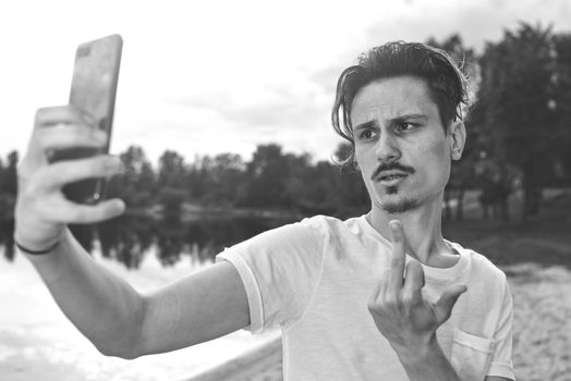 Portrait of angry confused aggressive in bad mood guy irritably speaks on the phone on the background of the lake