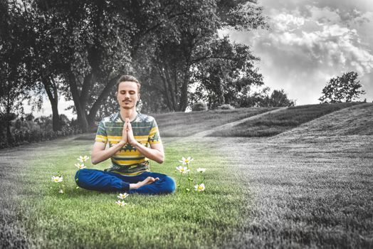 Young man meditating outdoors in the park, sitting with eyes closed and his hands together